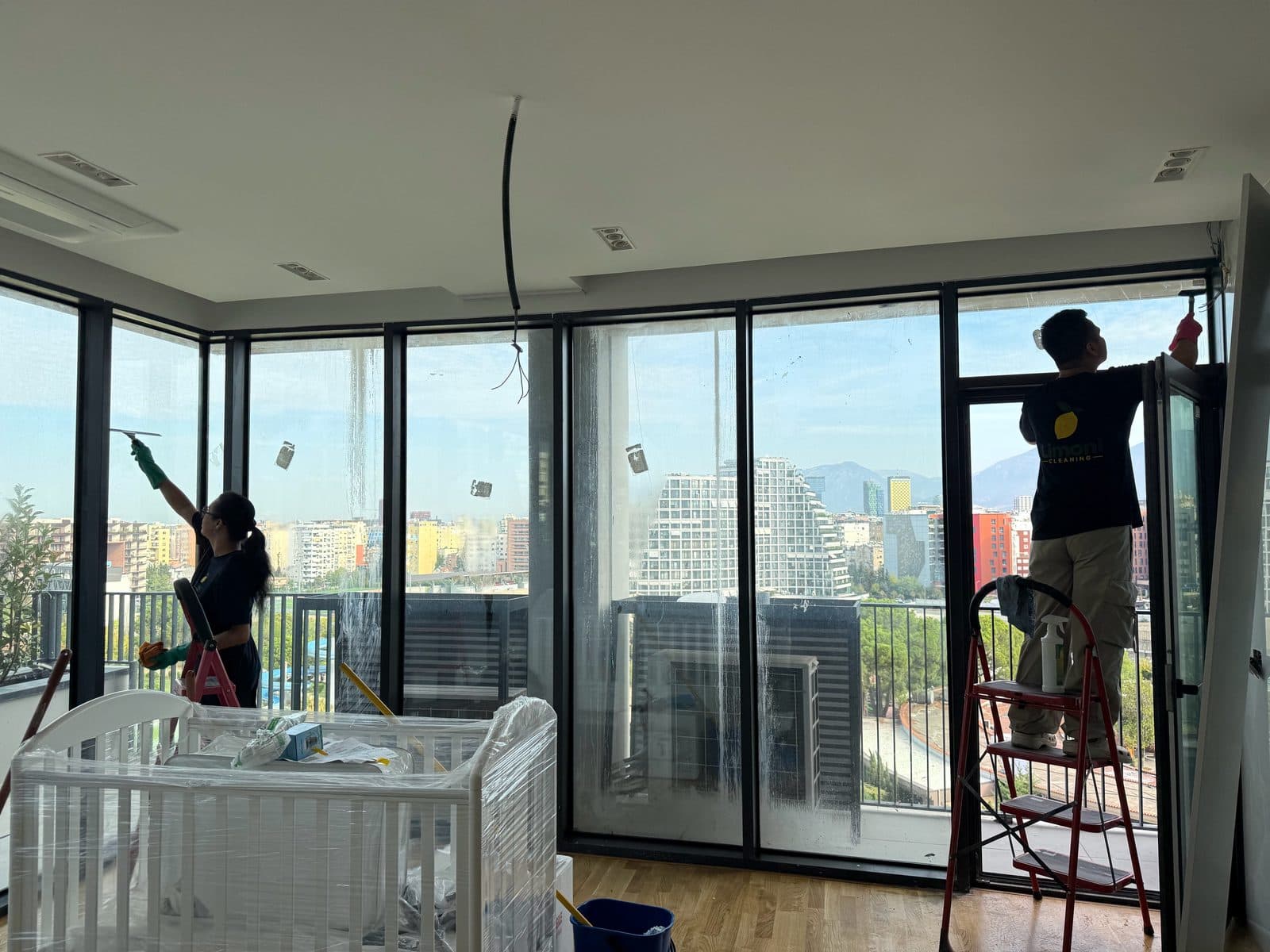 Dy punonjëse të Limoni Cleaning duke pastruar xhamat e mëdhenj të një apartamenti të ri pas punimeve në Tiranë