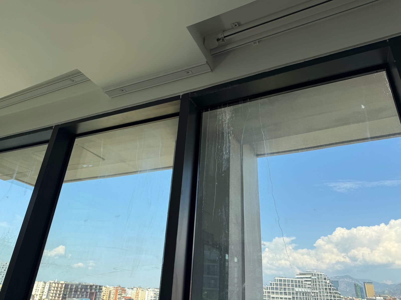 Xhamat e mëdhenj dhe kornizat e zeza të dritareve në një apartament të ri në Tiranë